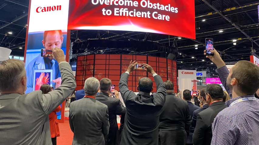 A crowd of attendees capturing video of Canon's unveiling of two new AI-enabled CT systems at during RSNA 2023. Photo by Dave Fornell. #RSNA #RSNA23 #RSNA2023