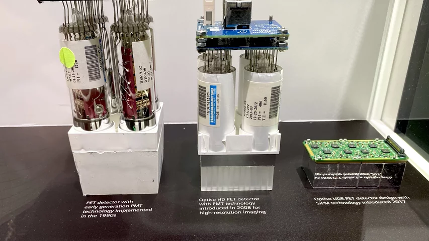 Display at Siemens showing the evolution from PET photo-multiplier tube detectors to much more compact and efficient digital detector technology between the 1990s to the latest system displayed at RSNA 2023. The small electronic board on the right is Siemen's current SiPM technology.Photo by Dave Fornell. #RSNA #RSNA23 #RSNA2023