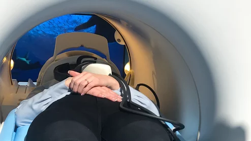 RSNA attendee tries out the new Philips 5300 MRI system video viewing system (projected on the wall behind the MRI and viewed using a mirror) to entertain patients during longer exams. The system is a "helium free" system. It has a seals cooling system so it only uses 7 liters of helium, as opposed to the usual 1,500 liters in conventional MRI systems.